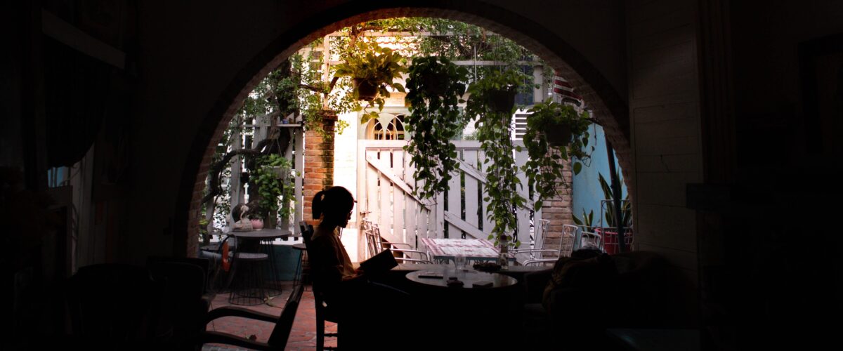 Woman sitting alone on a patio reading a book, surrounded by plants, enjoying her alone time, how to access your inner voice