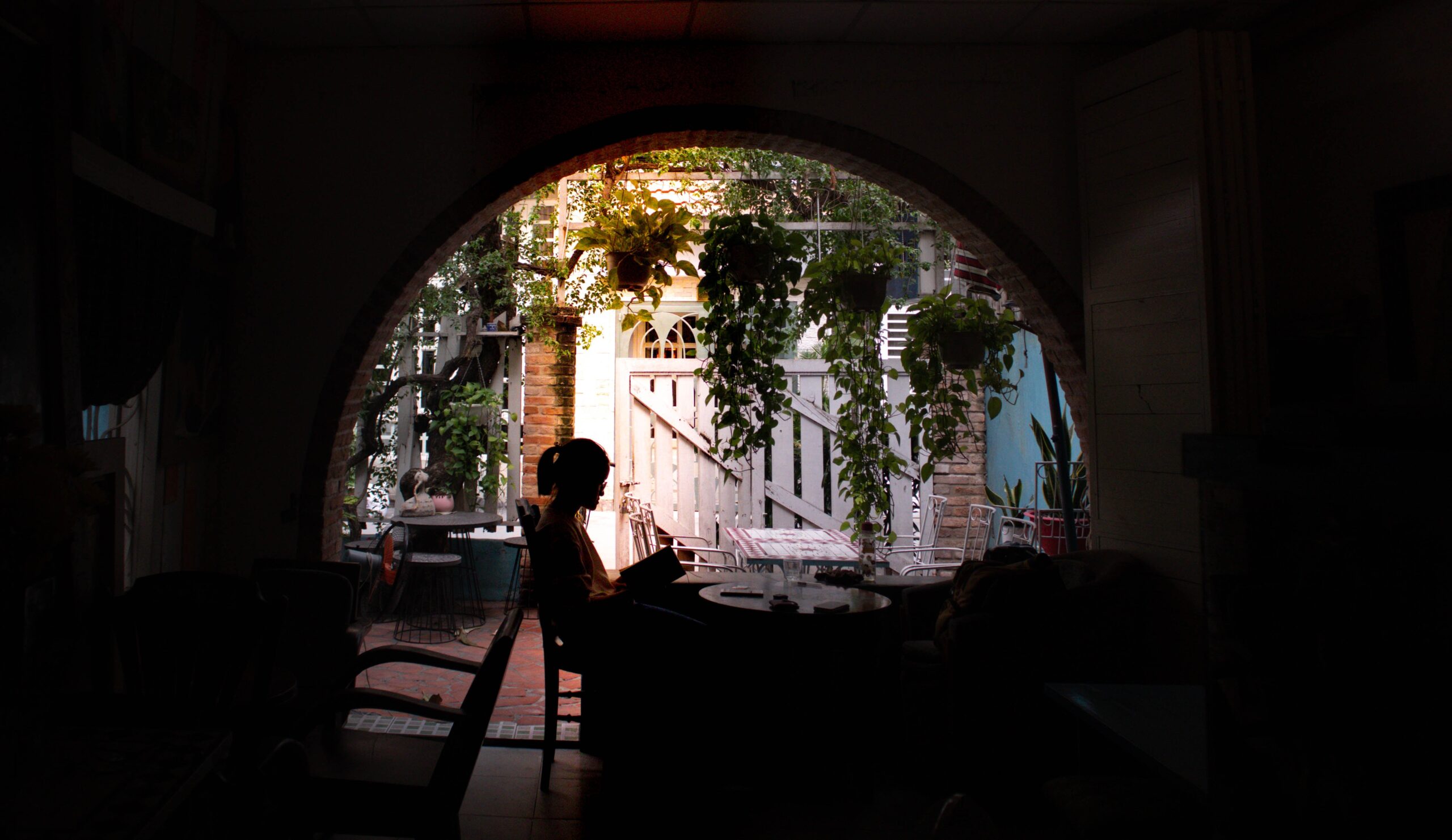 Woman sitting alone on a patio reading a book, surrounded by plants, enjoying her alone time, how to access your inner voice